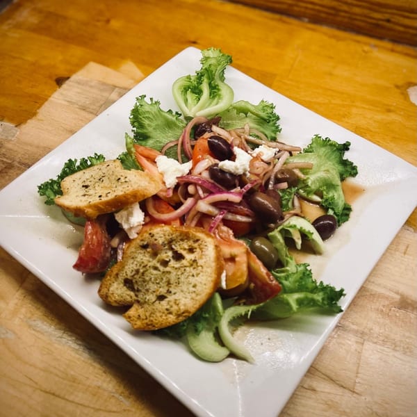 Fresh Greek salad with lettuce, tomatoes, olives, red onions, feta cheese, and croutons on a white plate.