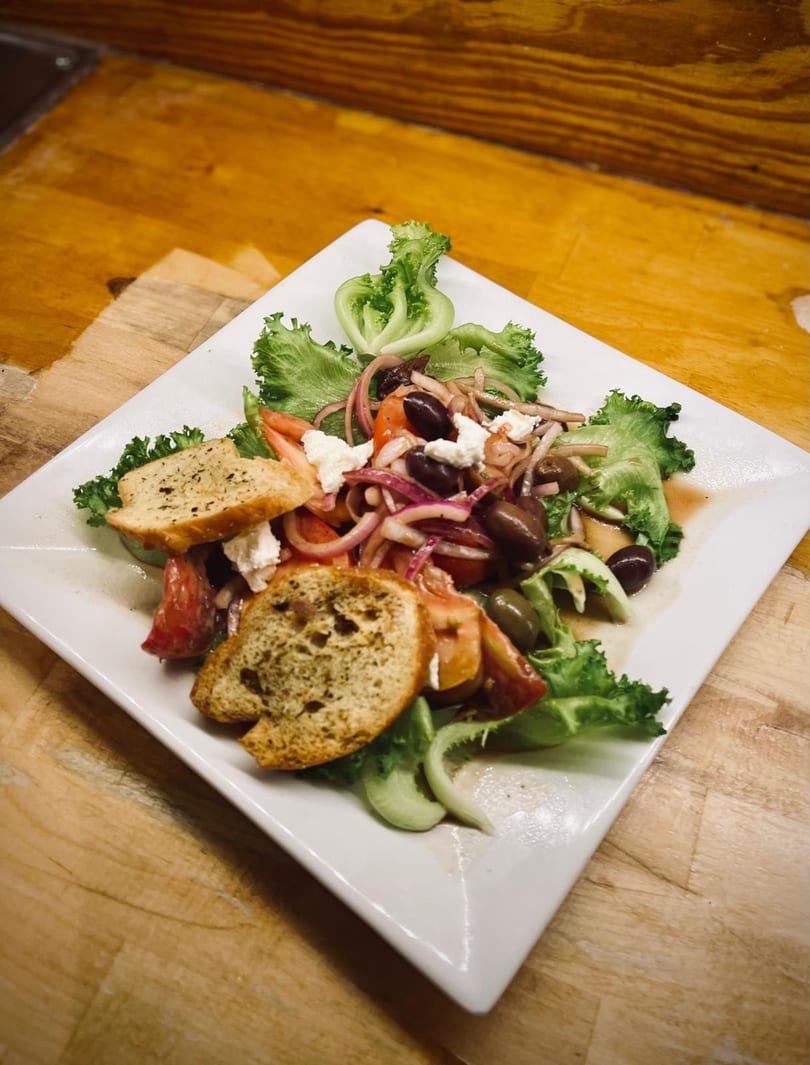 Fresh Greek salad with lettuce, tomatoes, olives, red onions, feta cheese, and croutons on a white plate.
