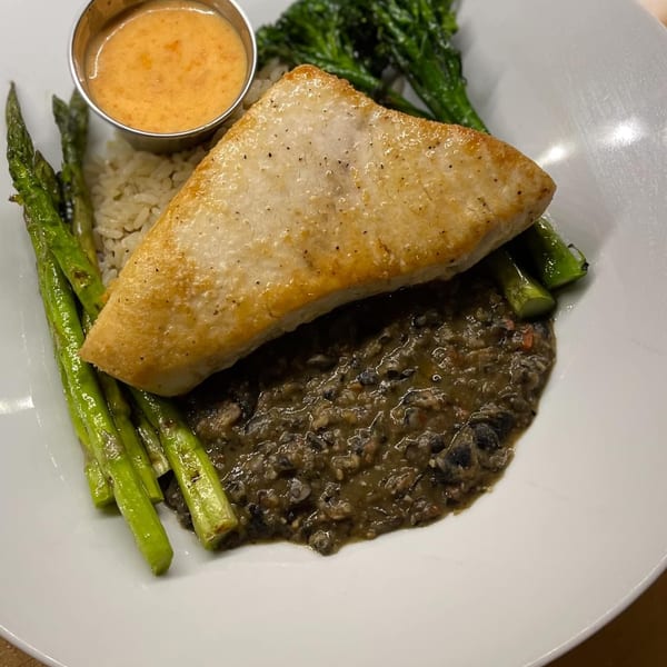 Pan-seared fish with rice, black beans, asparagus, broccolini, and a side of sauce.