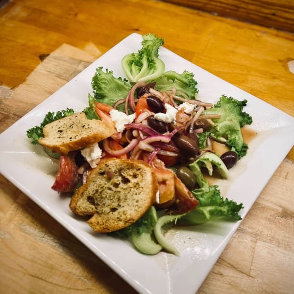 A vibrant salad with lettuce, tomatoes, red onions, olives, feta, and croutons on a white plate.