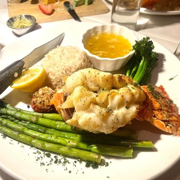Lobster tail with asparagus, rice, lemon, and melted butter on a white plate.