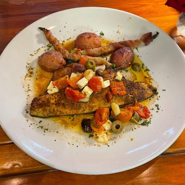Blackened fish with cherry tomatoes, feta, olives, and roasted potatoes on a white plate.