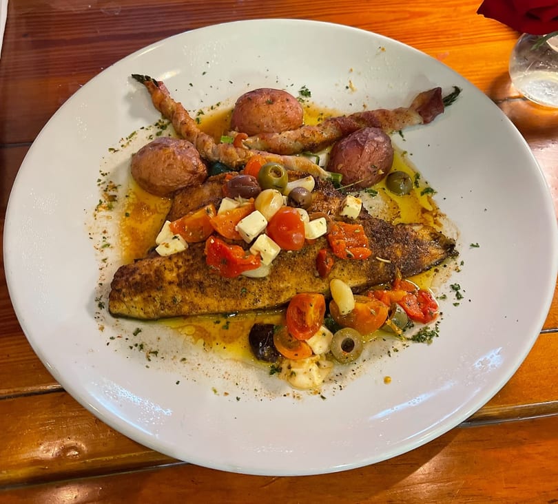 Blackened fish with cherry tomatoes, feta, olives, and roasted potatoes on a white plate.
