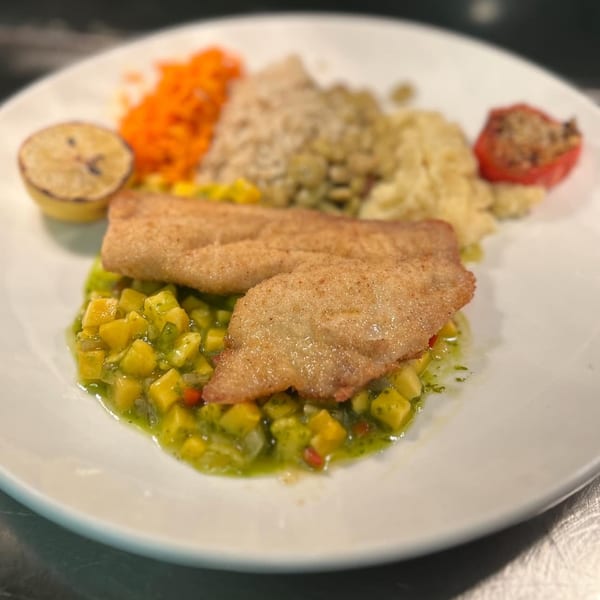 Pan-fried fish fillets on mango salsa, with sides of rice, mashed potatoes, carrots, and a lemon.