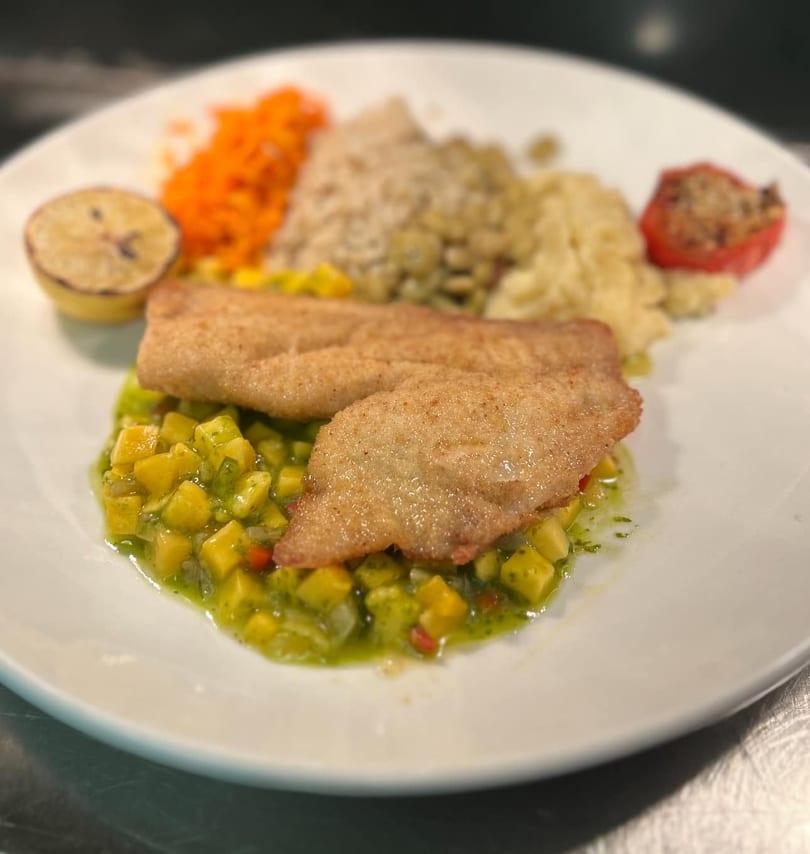 Pan-fried fish fillets on mango salsa, with sides of rice, mashed potatoes, carrots, and a lemon.