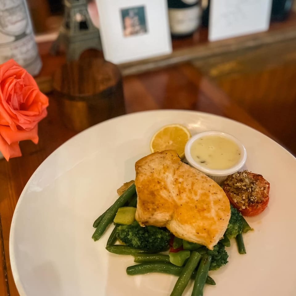 Grilled chicken breast with green beans, broccoli, roasted tomato, lemon, and a side of sauce.