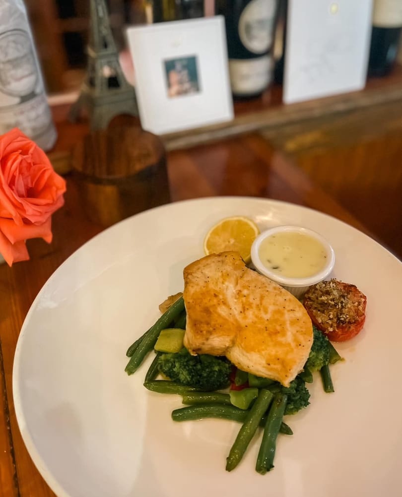 Grilled chicken breast with green beans, broccoli, roasted tomato, lemon, and a side of sauce.