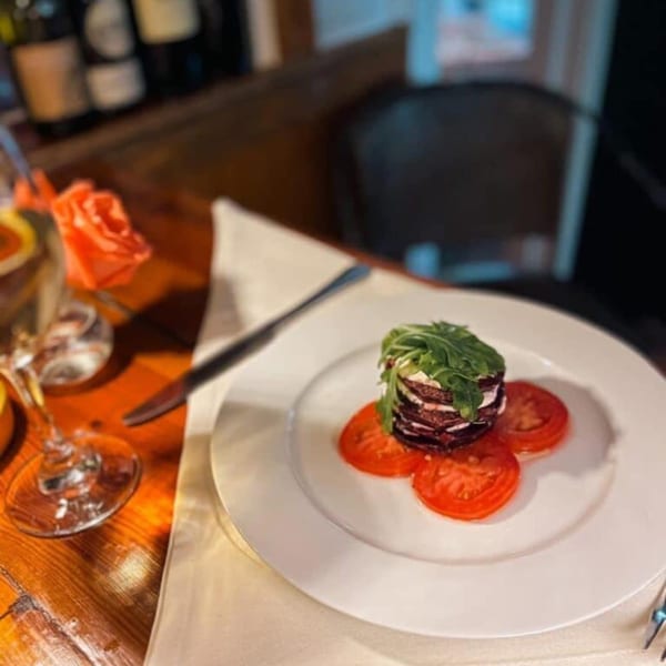 Beetroot and goat cheese stack with arugula and tomato slices on a white plate.