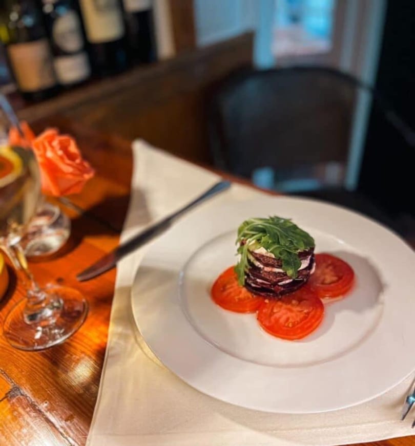 Beetroot and goat cheese stack with arugula and tomato slices on a white plate.