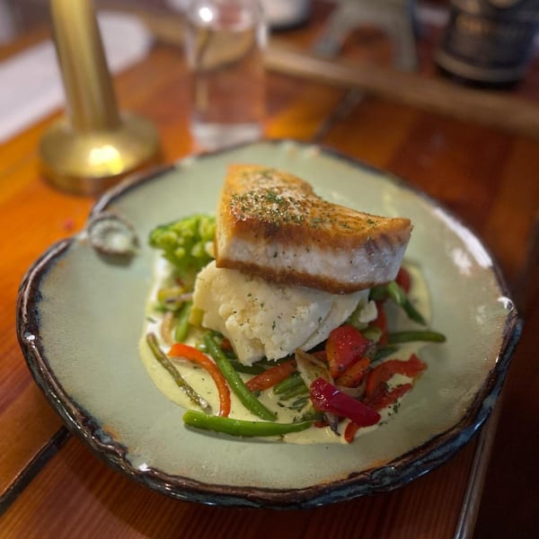 Seared fish on mashed potatoes with green beans and red peppers in a creamy sauce.