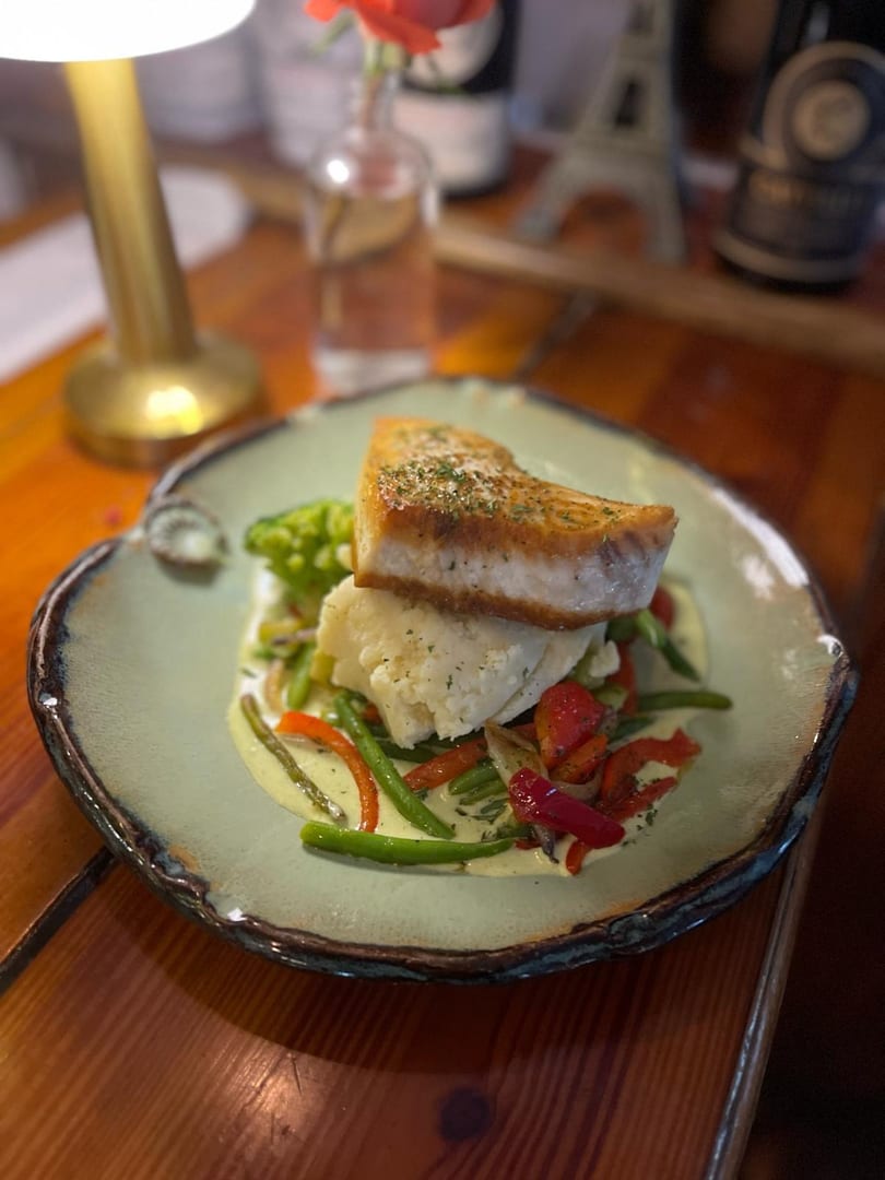 Seared fish on mashed potatoes with green beans and red peppers in a creamy sauce.