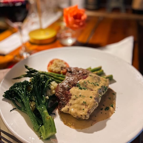 Ribeye steak with brandy demi-glaze, broccolini, asparagus, and a baked tomato on a white plate.