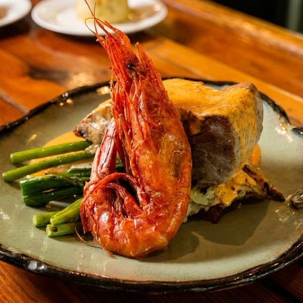 A large grilled prawn, asparagus, and a piece of meat with sauce on a plate.