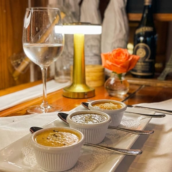Three small bowls of soup on a white tray, with a wine glass and decor in the background.